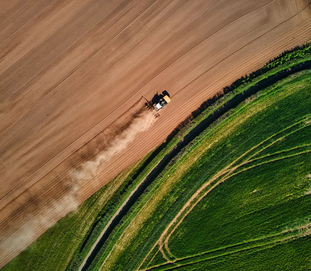 Aerial view of a tractor plowing a field, creating contrast between the tilled soil and the surrounding greenery.